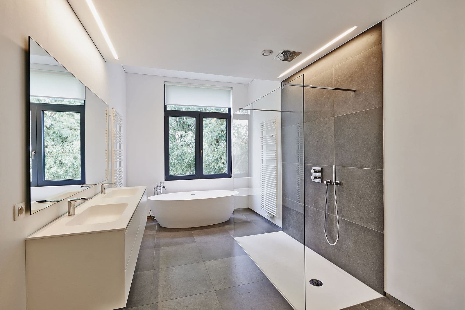 Modern bathroom with a freestanding tub by a large window, double sink vanity, and a glass-enclosed shower. Neutral tones create a serene feel.